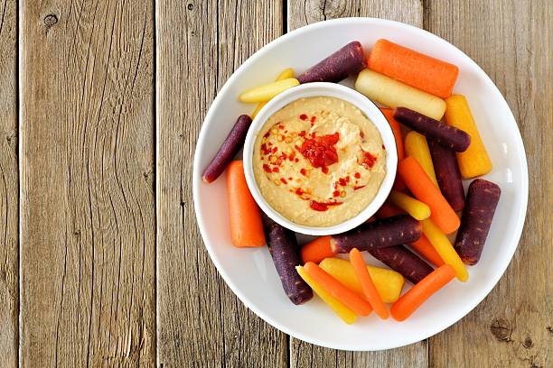 Plate of baby rainbow carrots with hummus on rustic wood