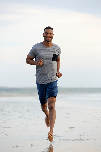 Smiling young man running barefoot at the beach