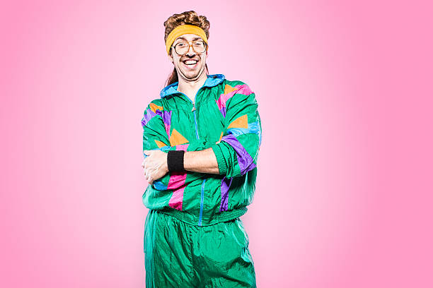 Mullet Man With Eighties Fashion Style A cool, funky young adult in late 1980's / early 1990's fashion style, with mullet, fluorescent colored track suit, nerdy glasses, and sweat band.  He smiles at the camera with a cheesy grin, his arms folded. Vibrant pink background. Horizontal with copy space. 1980s style stock pictures, royalty-free photos & images