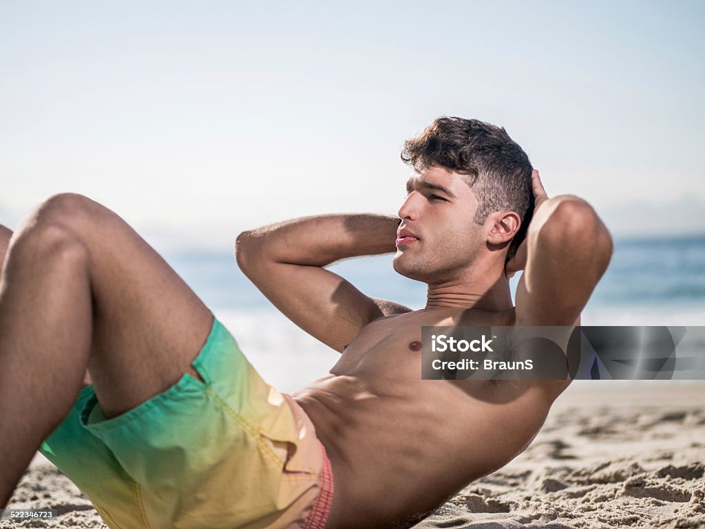 Hombre haciendo sit ups en la playa. - Foto de stock de Abdominales libre de derechos