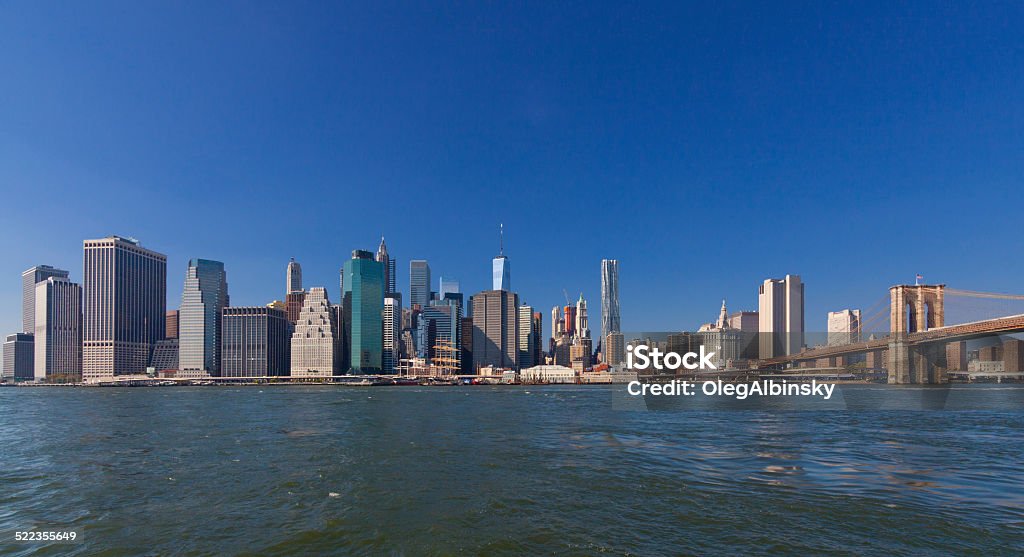 New York Skyline with World Trade Center and Brooklyn Bridge. Wide angle view of Financial District of Manhattan Lower East Side as seen from the Brooklyn Bridge Park on a beautiful autumn day, New York City. The World Trade Center tower is in the center and Brooklyn Bridge is in the right part of the image. American Flag Stock Photo