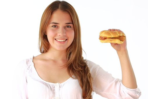 Closeup of a young lady showing her hamburguer like saying that she eats hamburguers but still she is fit and beautiful. This is a studio shot over white background