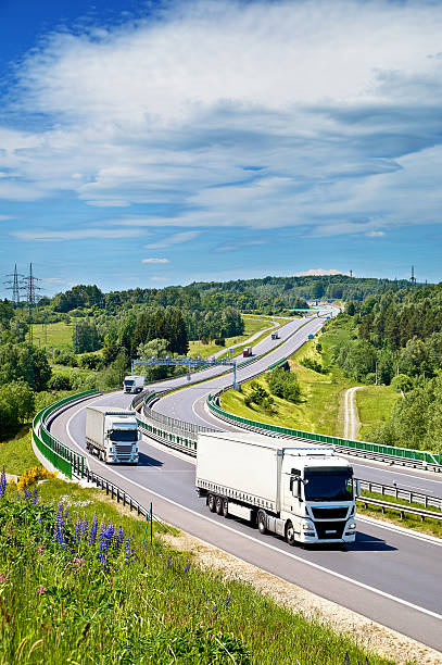 White trucks drive along an asphalt highway in a landscape.