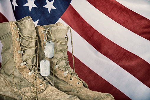 Old combat boots and dog tags with American flag in the background. Vintage filter effects.