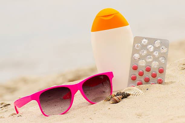 Pink sunglasses, shells, sun lotion and pills of vitamin E on sand at the beach, seasonal concept and successful tanning