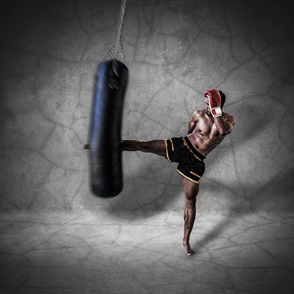 thai boxer character is kicking the sand bag on concrete wall background closeup