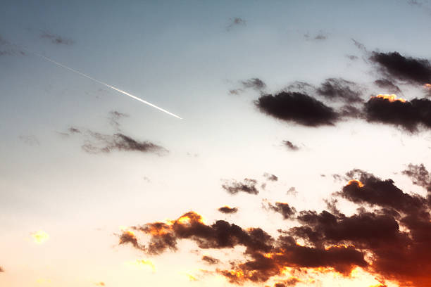 Jet with vapor trail flying toward a dramatic sunset.