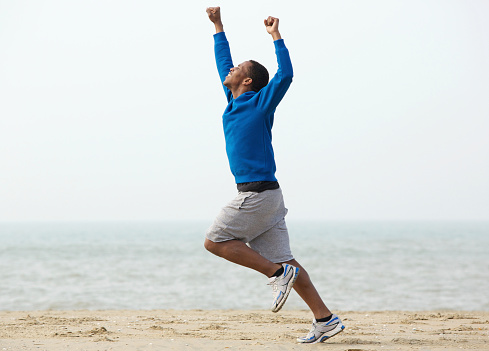 Young black man running at the beach with arms raised in victory