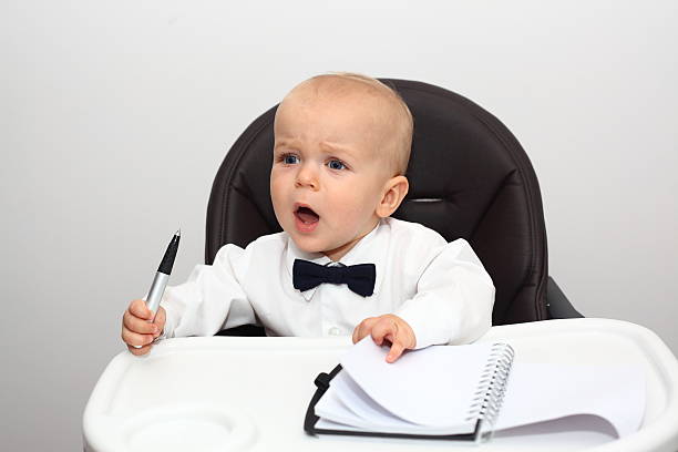 Angry baby boss A cute Caucasian baby sitting in his high chair wearing a white shirt and a bow tie looking like a boss with pen and paper and yelling at somebody. Baby boss yelling at his subordinates. Funny little businessman. See more in my portfolio bossy stock pictures, royalty-free photos & images