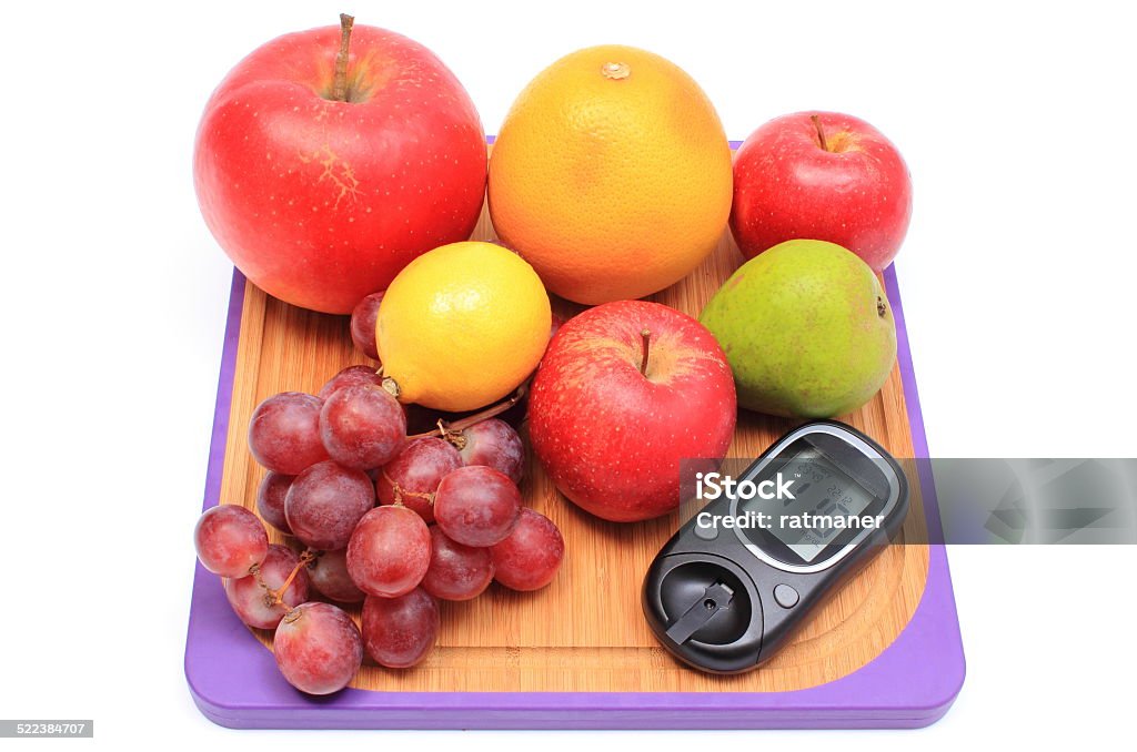 Fresh natural fruits with glucose meter on cutting board Fresh ripe natural fruits and glucometer lying on wooden cutting board, concept for healthy eating and diabetes Apple - Fruit Stock Photo