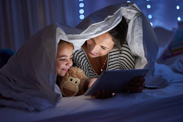 Bedtime meets playtime Shot of a mother using a digital tablet with her daughter under a blanket fort bedtime photos stock pictures, royalty-free photos & images