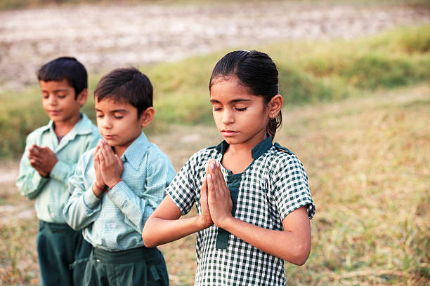 Group of little children standing in the field wearing school uniform & praying to the god.