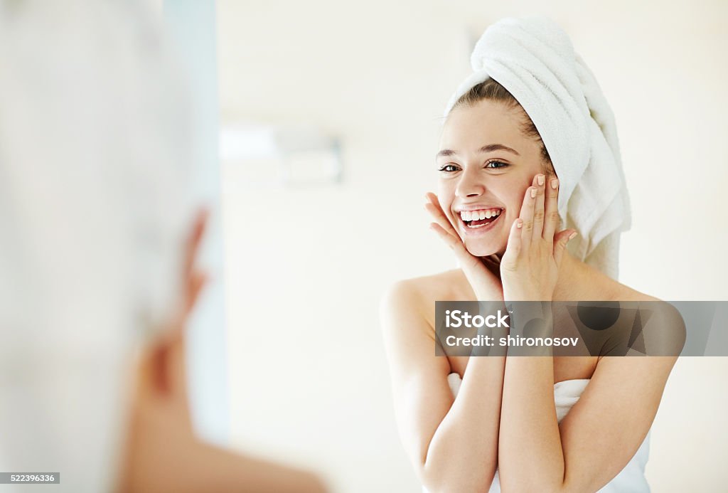 Facial care Happy girl looking at her face in mirror after bath Women Stock Photo