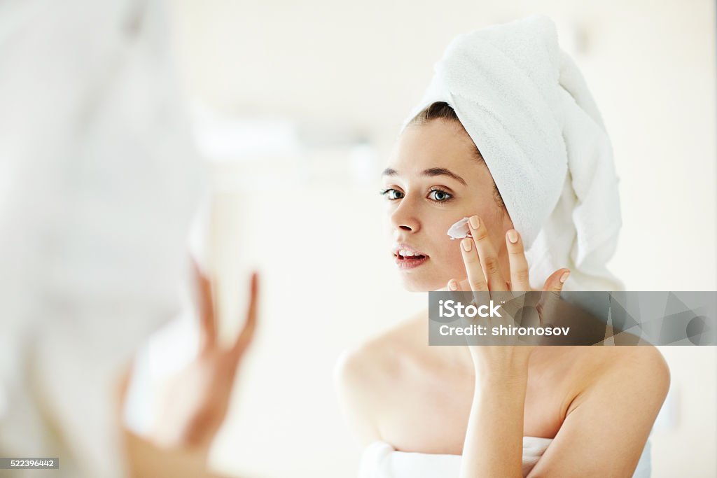 Pampering cream Pretty girl applying moisturizing cream in front of mirror Moisturizer Stock Photo