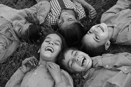 Group of cheerful children wearing school uniform lying down on grass & laughing elevated view.