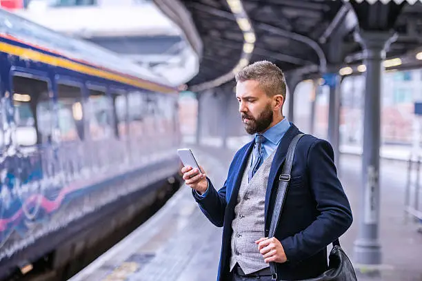 Photo of Hipster businessman with smartphone, waiting at the train platfo