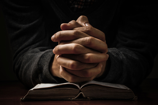 Hands of a man praying in solitude with his Bible.