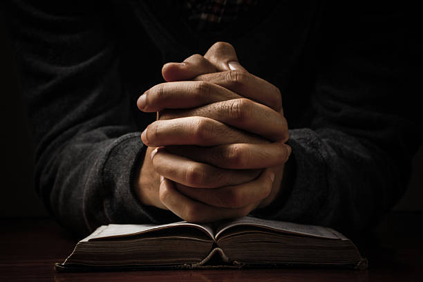 Praying Hands With Bible Hands of a man praying in solitude with his Bible. prayer stock pictures, royalty-free photos & images