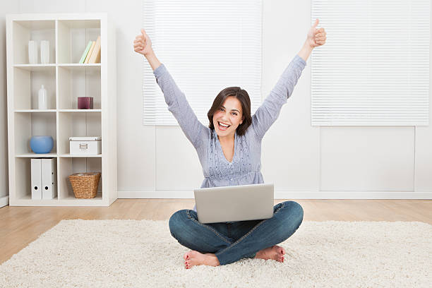 istock Woman Raising Arms While Using Laptop On Rug 522403189