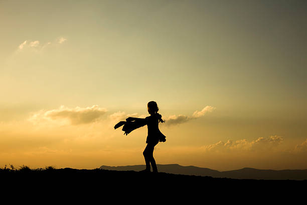 istock Little Girl Playing with her Coat Silhouetted by Setting Sun 522404495