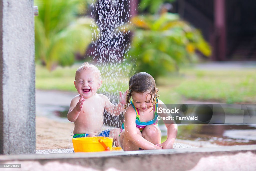 Happy kids in an outdoor shower Two happy children, adorable baby boy and a little toddler girl in swimming suits playing in an outdoor shower in a tropical reasort during summer vacation Asia Stock Photo