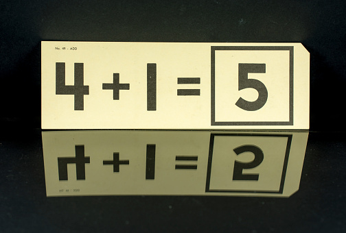 Old elementary school math flash cards on a black background reflected on glass. 4+1= 5
