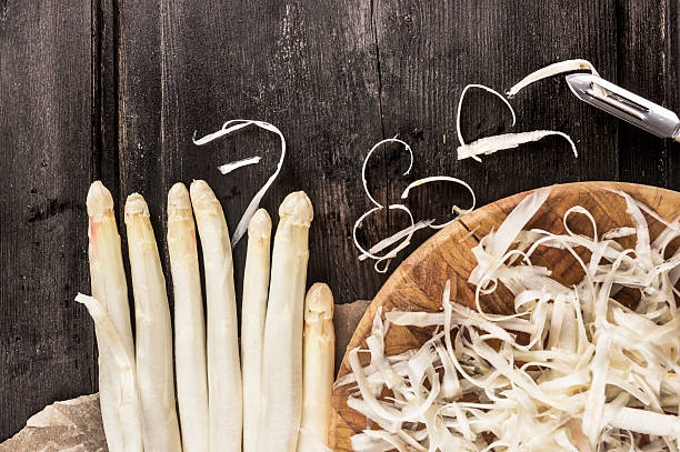 Shelled white asparagus with peelings on dark wooden table stock photo