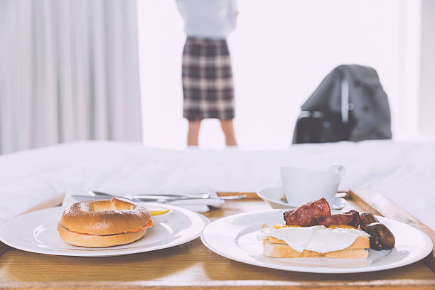 asian businesswoman standing by window, breakfast on the bed  in the morning at  hotel, business trip on the road. Focus on the food.