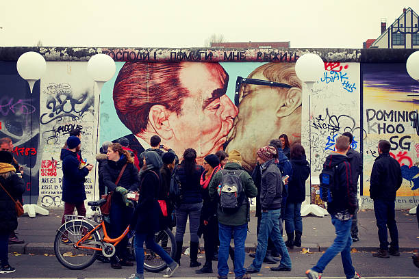 Socialist fraternal kiss Berlin, Germany - November 9, 2014: Socialist fraternal kiss, you can see the Graffiti painting from 1990 on the Berlin Wall called "My God, Help Me to Survive This Deadly Love". Tourists walking along the East Side Gallery, an international memorial for freedom with 105 paintings by artists from all over the world on a 1,3 km long section of the Berlin Wall. friedrichshain photos stock pictures, royalty-free photos & images