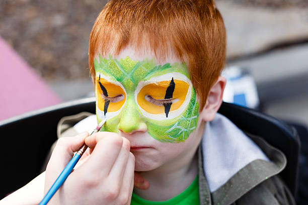 A portrait of a young boy having a mask painted onto his face.