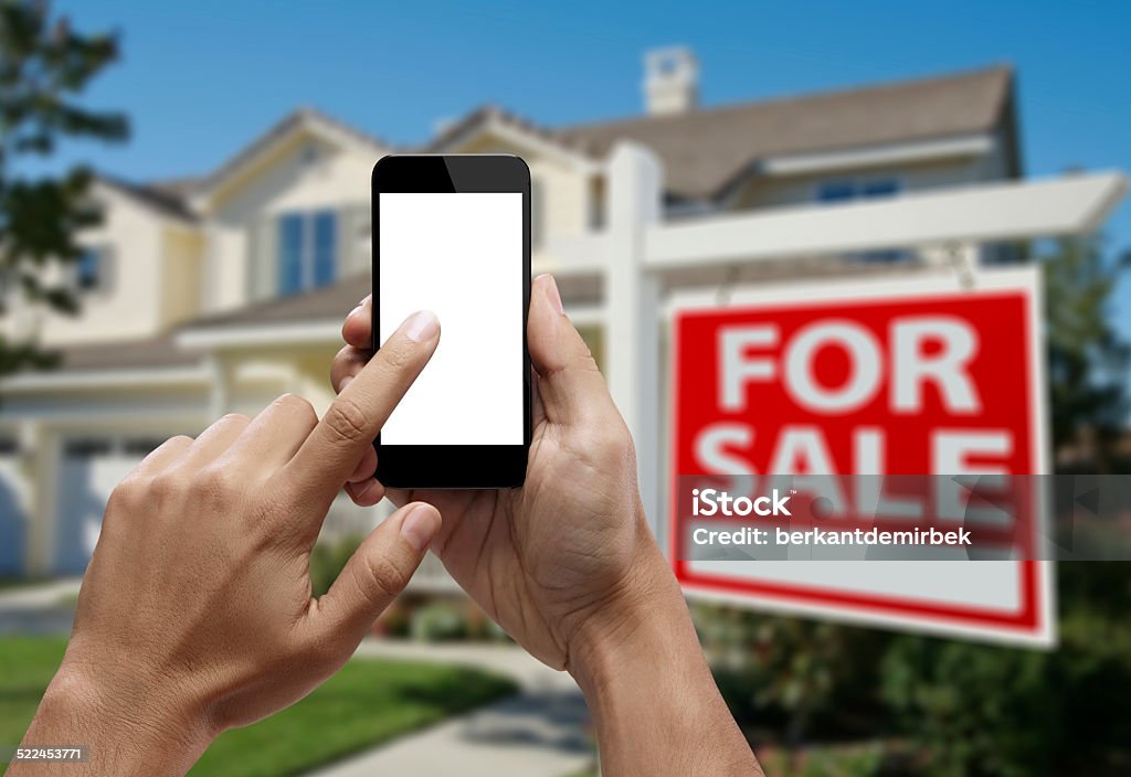 Hand holding smartphone with index finger touching the screen Hand holding smartphone with forefinger touching the screen and house background. Choice Stock Photo