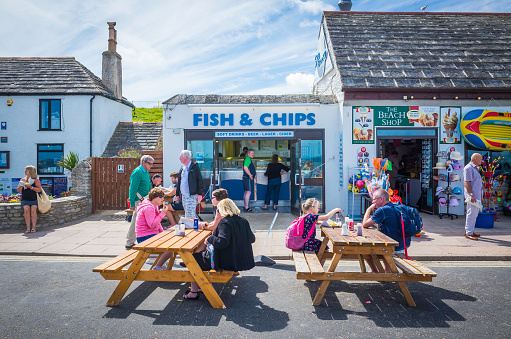 Swanage, UK - August 6, 2015: Holiday makers and tourists enjoying the summer sunshine at table outside a traditional British fish and chip shop on the beach promenade at the popular seaside resort of Swanage, Dorset, UK. 