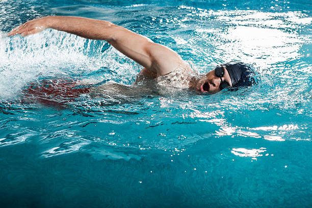 jeune homme à nager le crawl dans une piscine - blue construction built structure indoors photos et images de collection