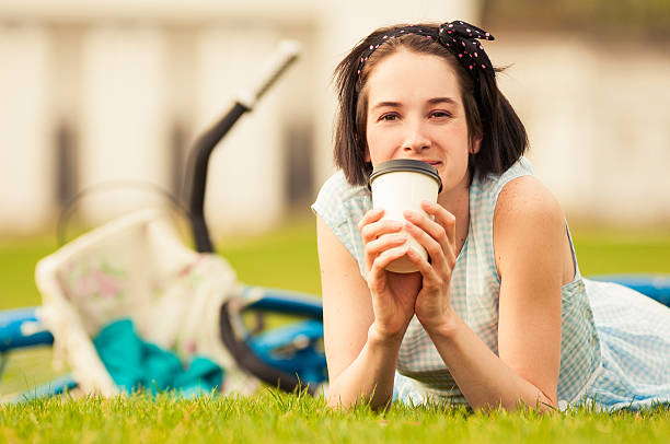 istock Happy female with coffee cup lying on grass 522459542