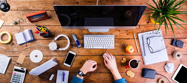 Business person working at office desk. Smart watch on hand and smart phone on the table. Coffee cup, notepad and glasses and various office supplies around the workplace. Flat lay.