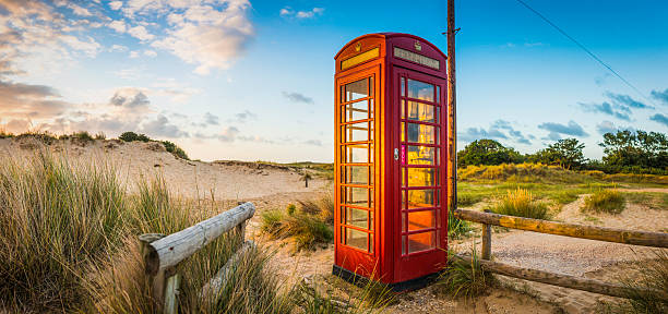 British red telephone box illuminated at sunrise on seaside beach Red telephone box set amongst the golden sand dunes of a summer seaside beach illuminated by the warm sunlight of daybreak. ProPhoto RGB color profile for maximum color gamut. bournemouth england photos stock pictures, royalty-free photos & images