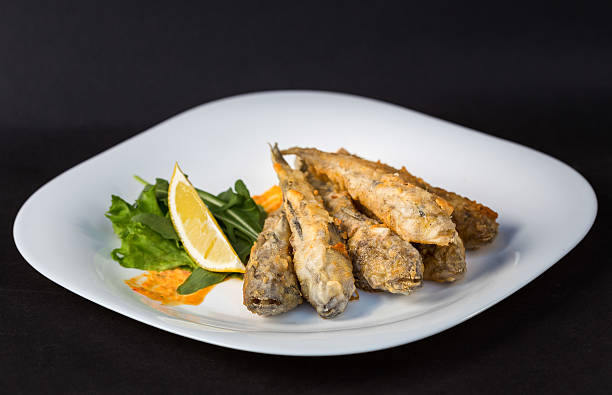 Fried fish gobies in batter with lemon and greens Fried fish gobies in batter with lemon and greens on white plate against black background bullhead fish stock pictures, royalty-free photos & images