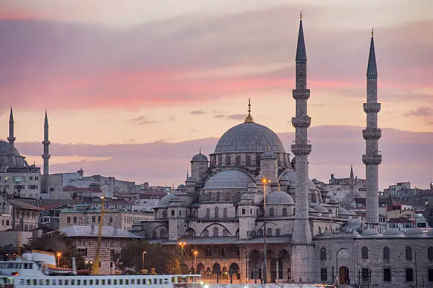 This vertical scenic view features the Yeni Cami, also known as the New Mosque, which is a famous architectural landmark that is located near Eminonu in the Fatih area of Istanbul, Turkey. The sunset sky is yellow with pink and purple wispy clouds. Photographed with a Nikon D800 during the 2014 Istanbul iStockalypse.