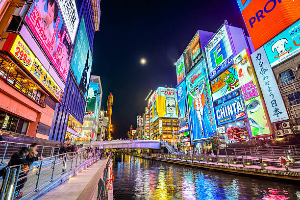 Osaka, Japan at Dotonbori Canal Osaka, Japan - November 25, 2012: Tourists observe the famed advertisements of Dotonbori Canal. With a history dating from 1612, the district is now one of Osaka's primary tourist destinations. osaka city photos stock pictures, royalty-free photos & images