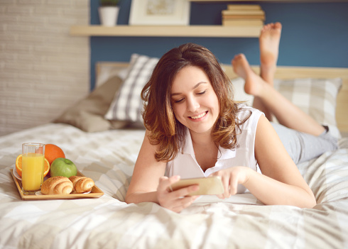 girl lying on the bed in the bedroom and using smartphone