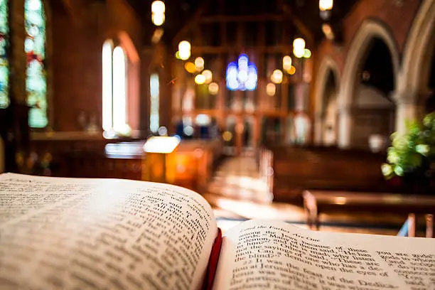 Bible open at the book of John inside an Anglican Church of England church. The focus is on the foreground of the bible, while in the background, defocused, are the pews and arches of the historic eighteenth century building. Horizontal colour image with copy space. 