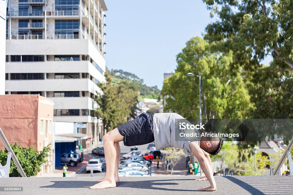 african man doing his daily yoga on the city bridge african male bending over in a yoga pose. He is doing his daily yoga on the bridge in the city. cape town, western cape, south africa Active Lifestyle Stock Photo