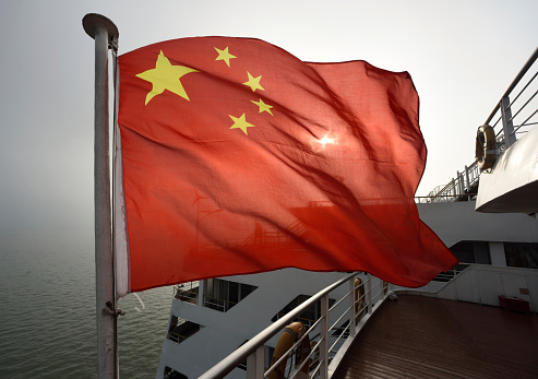 Backlit Chinese flag flying on the stern of a Yangtze River passenger ship, misty day.