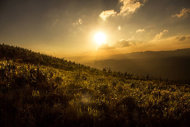 A DSLR photo taken from the top of Serra da Moeda, Minas Gerais, Brazil. Is is a beautiful sunny winter afternoon and the sun is low in the sky behind some white clouds, casting a warm light over the scene.