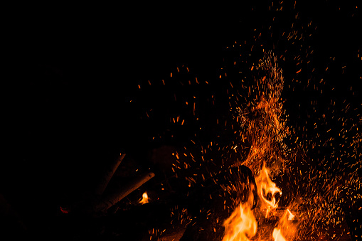 Sparks bounce off from a bonfire at night after a log thrown into it.
