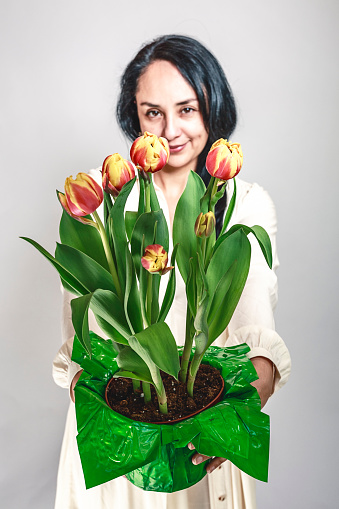A portrait of a beautiful latin woman with a tulips bouquet. Studio shot with light background.