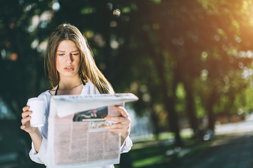 beautiful young woman reading the newspaper and drinking coffee