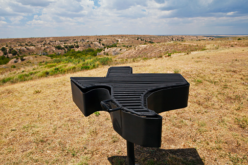 Texas shaped barbeque grill with rugged Texas panorama in background