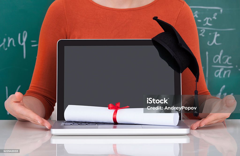 Student Showing Laptop With Mortarboard And Degree In Classroom Midsection of young college student showing laptop with mortarboard and degree in classroom Adult Stock Photo