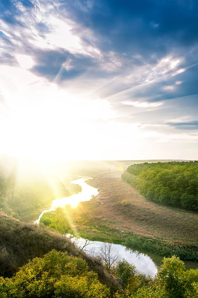 istock summer landscape on sunset with river, sun and cloudy sky. 522544035